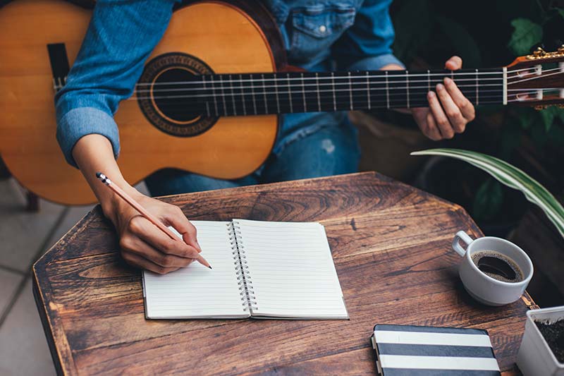 songwriting: man with guitar leaning over to write down lyrics he's working on